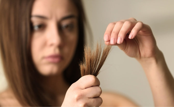 Woman looking worriedly at split ends, a clear sign that hair lacks nutrition and needs care from within