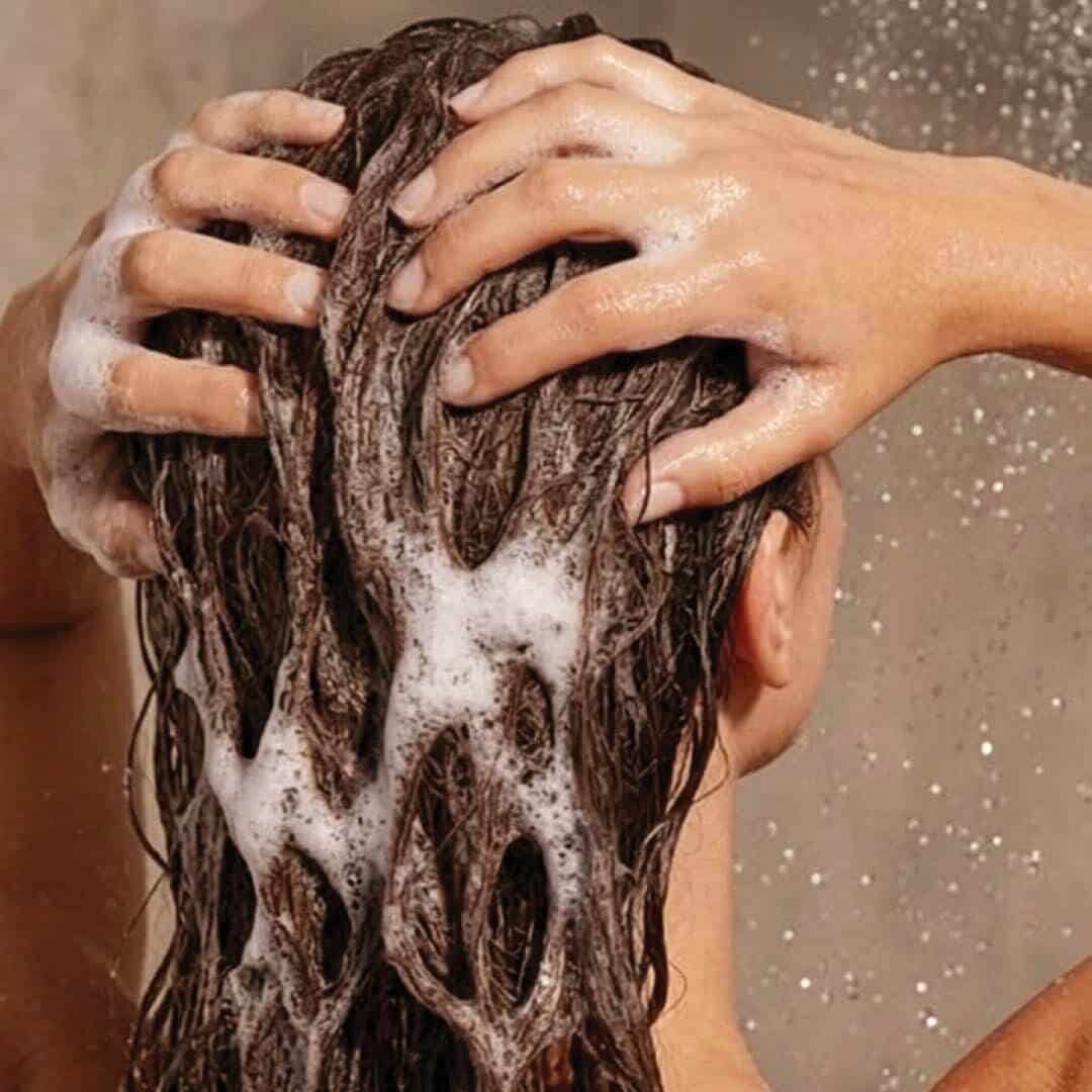 Woman massaging shampoo lather into her hair in the shower